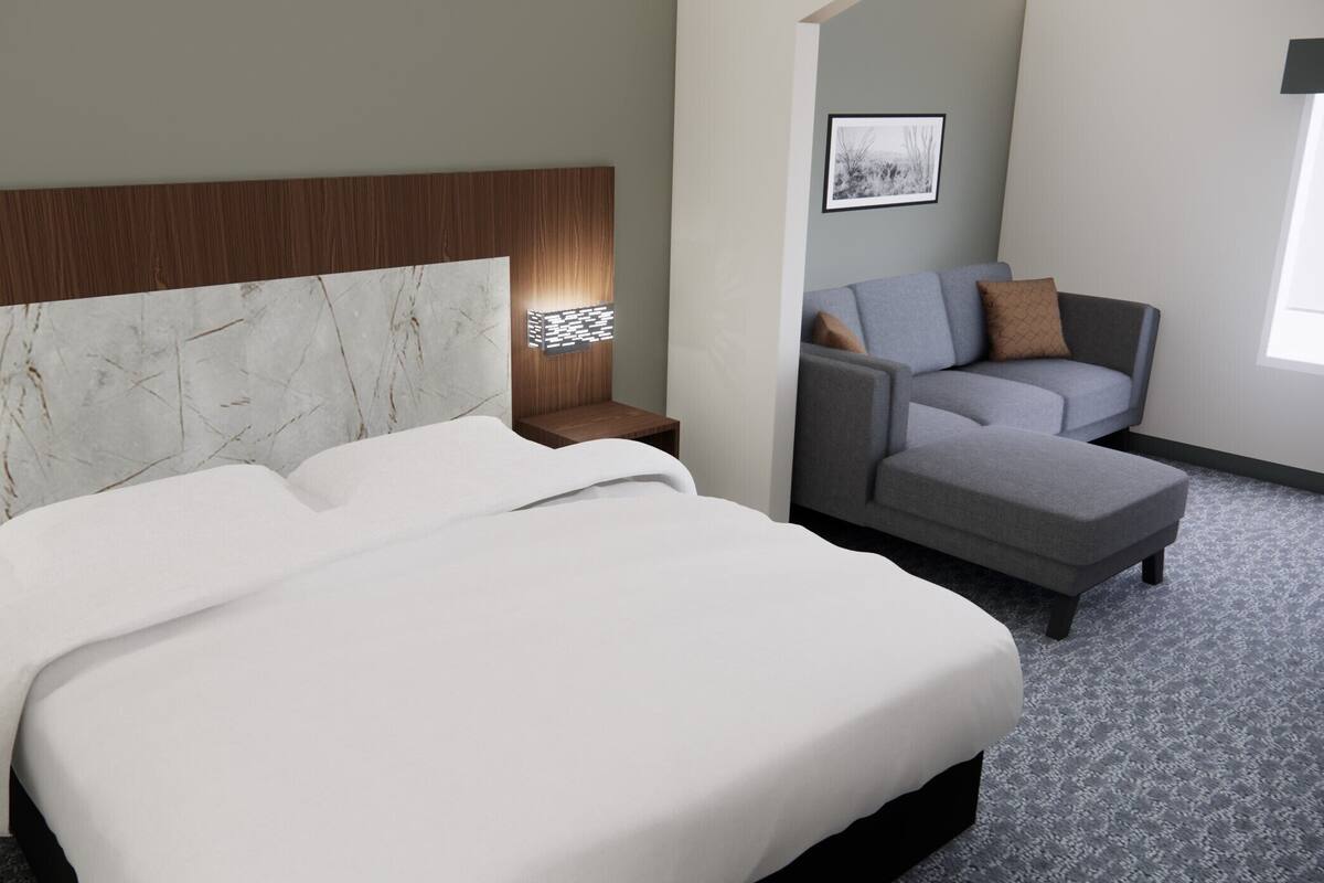 A hotel room with a large bed, a grey sofa, a small table, and a wall-mounted picture.