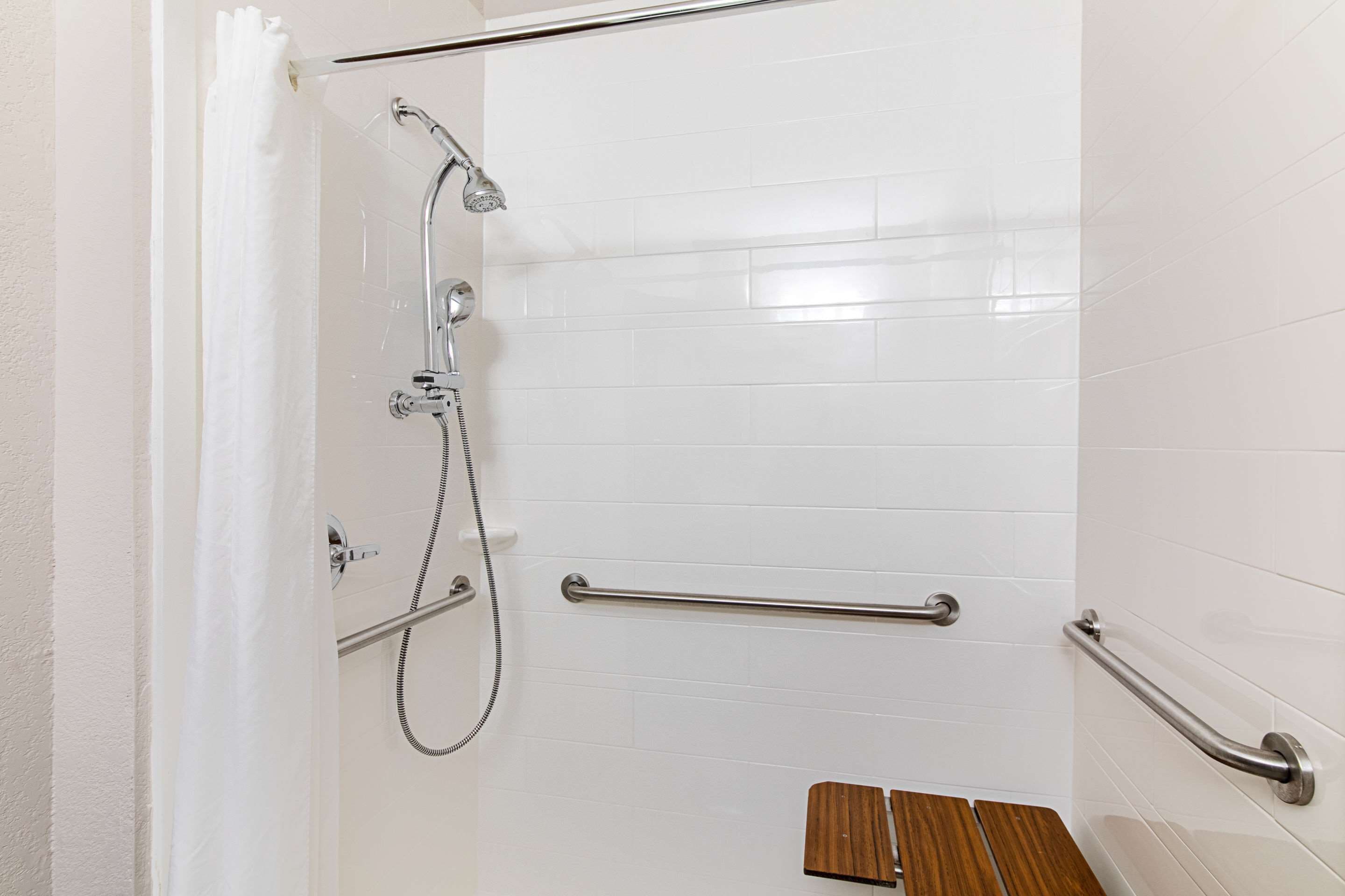 A shower with a handheld showerhead, grab bars, and a wooden bench.