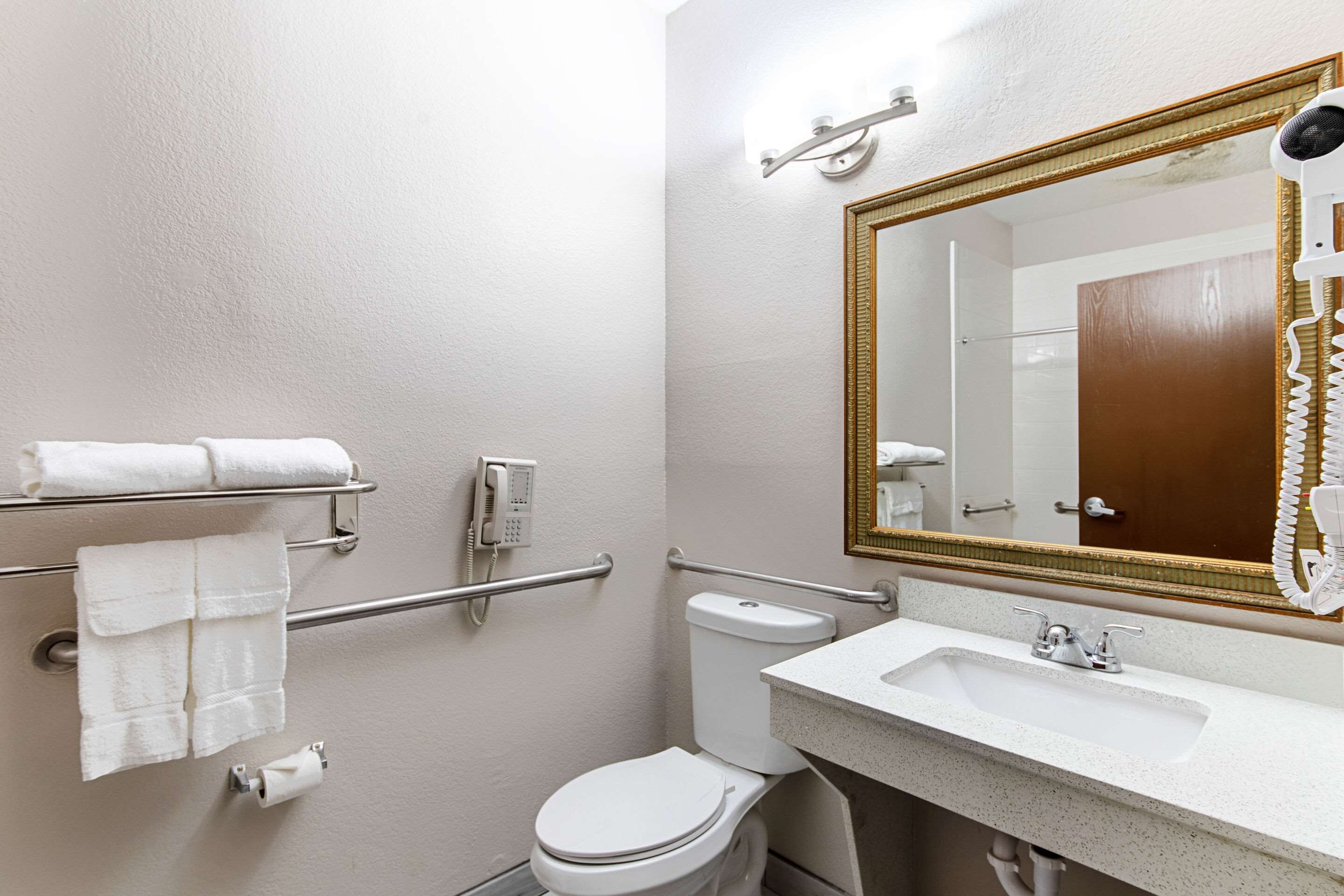 A bathroom with a white sink, toilet, and a large mirror. There are handrails on the walls and a towel rack with towels.
