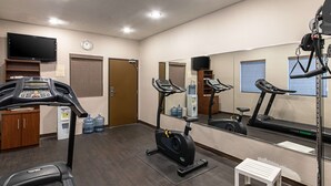 A gym with treadmills, an elliptical, a small white stool, a water cooler, and a television on the wall. - Quality Suites Austin South St. Elmo District (Austin)