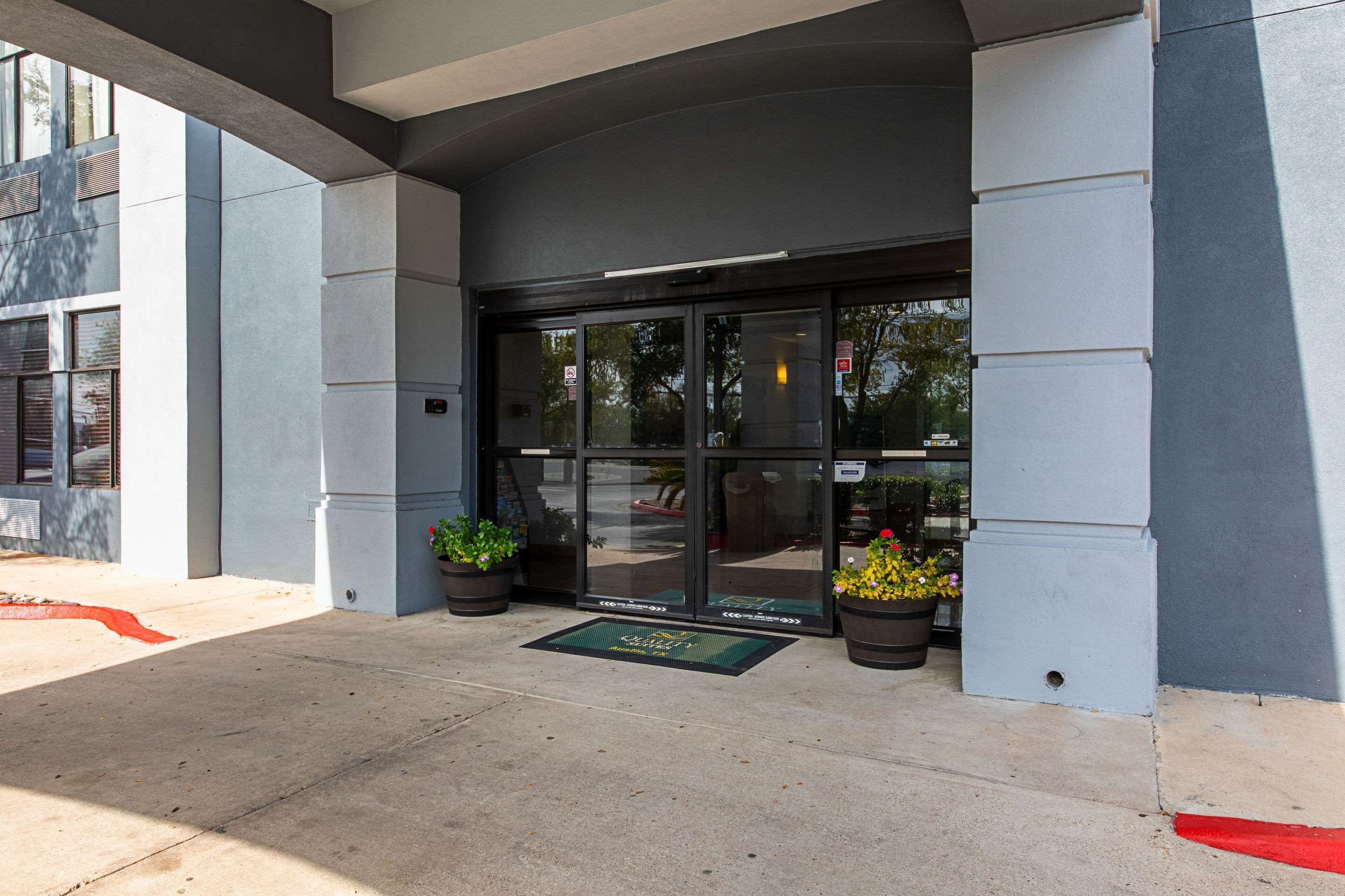 L’entrée d’un hôtel au design moderne, avec une porte en verre, un paillasson et des plantes en pot.