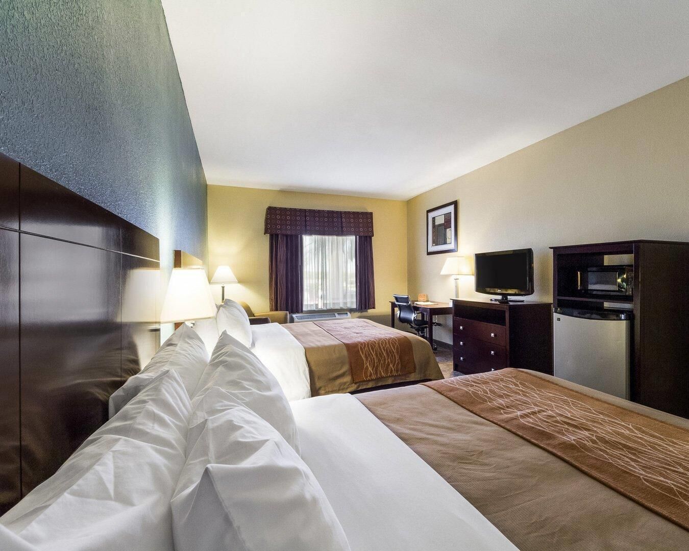 Habitación de hotel con dos camas, un escritorio, un televisor y un minibar.
