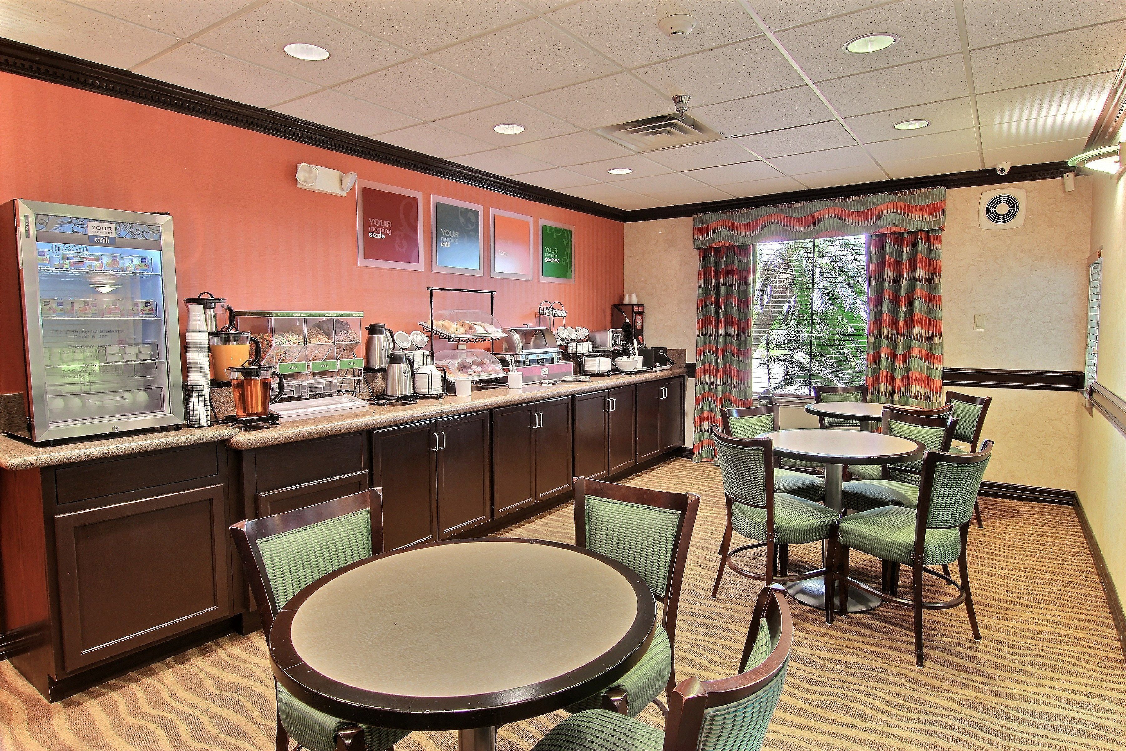 A hotel breakfast area with a self-service beverage machine, buffet, and seating area.