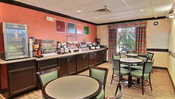 A hotel breakfast area with a self-service beverage machine, buffet, and seating area.