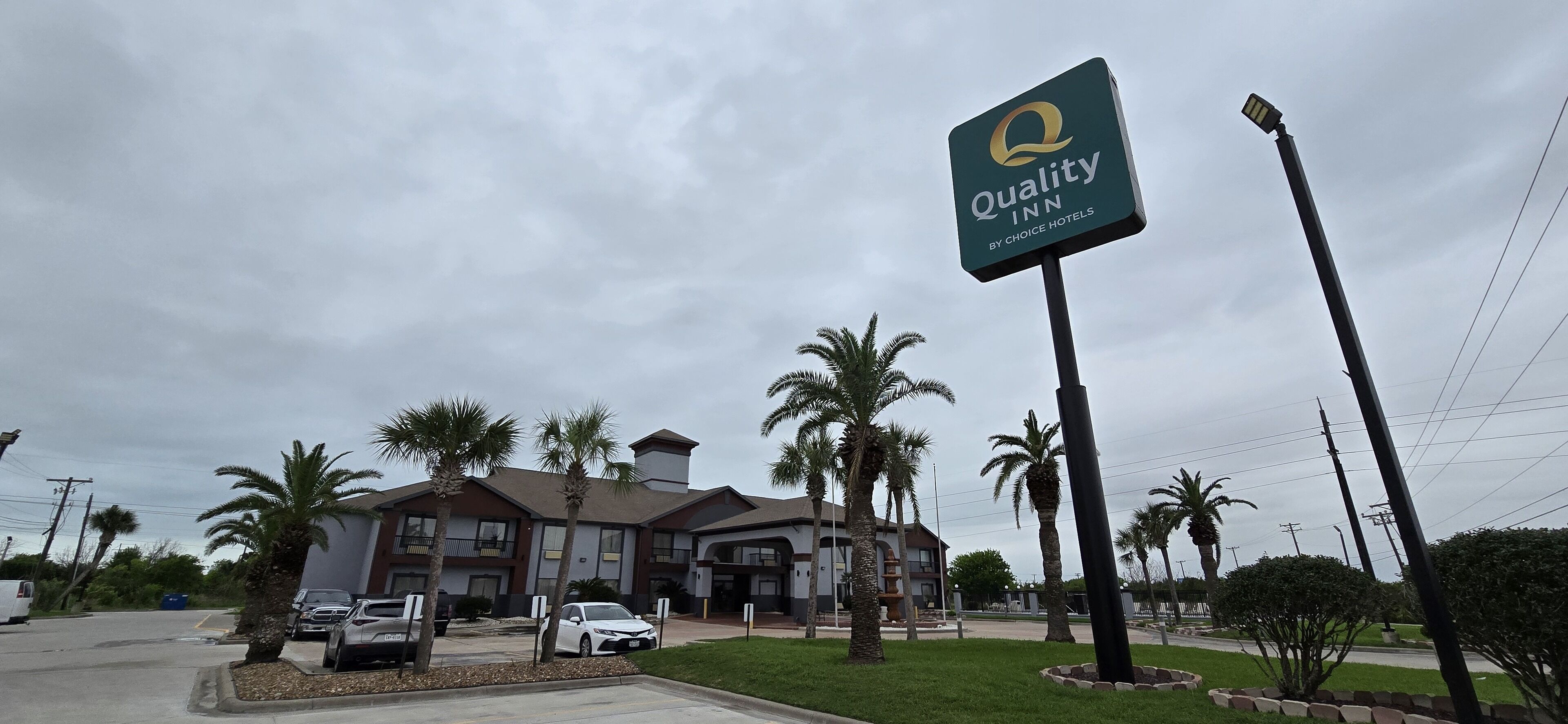 A Quality Inn by Choice Hotels with a large sign, palm trees, and a parking lot.