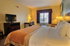 A hotel room with a large bed, a television, a desk, and two lamps.