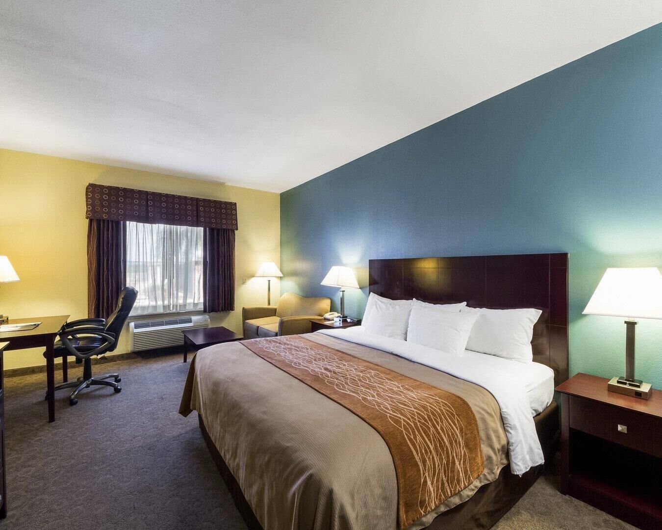 A hotel room with a bed, desk, chair, and two bedside lamps.
