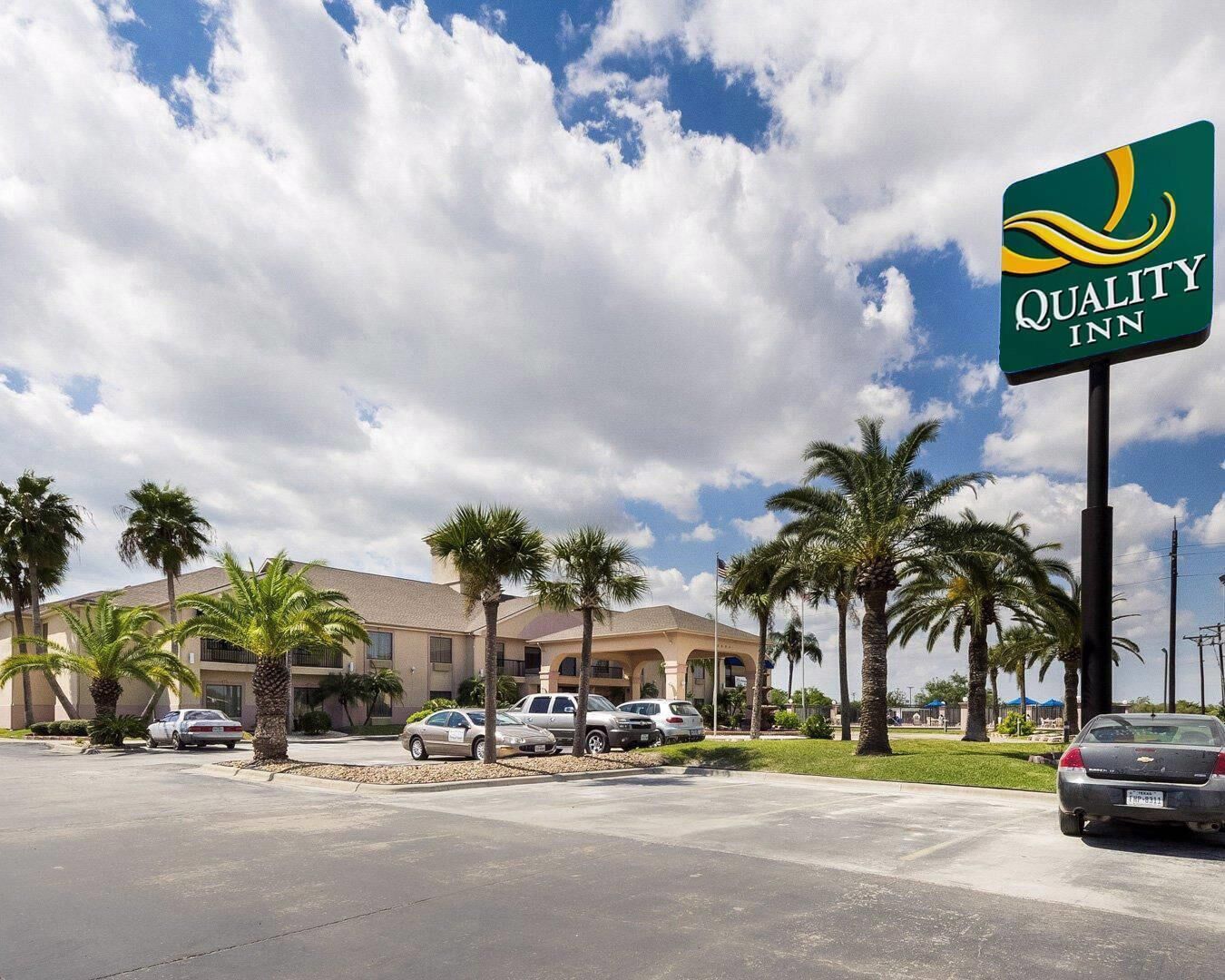 Um hotel Quality Inn com estacionamento, palmeiras e céu claro.