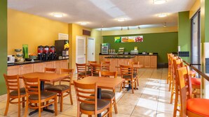 A bright and clean restaurant with wooden tables and chairs, a kitchen area, and a green wall with food images. - Quality Inn at Arlington Highlands (Arlington)