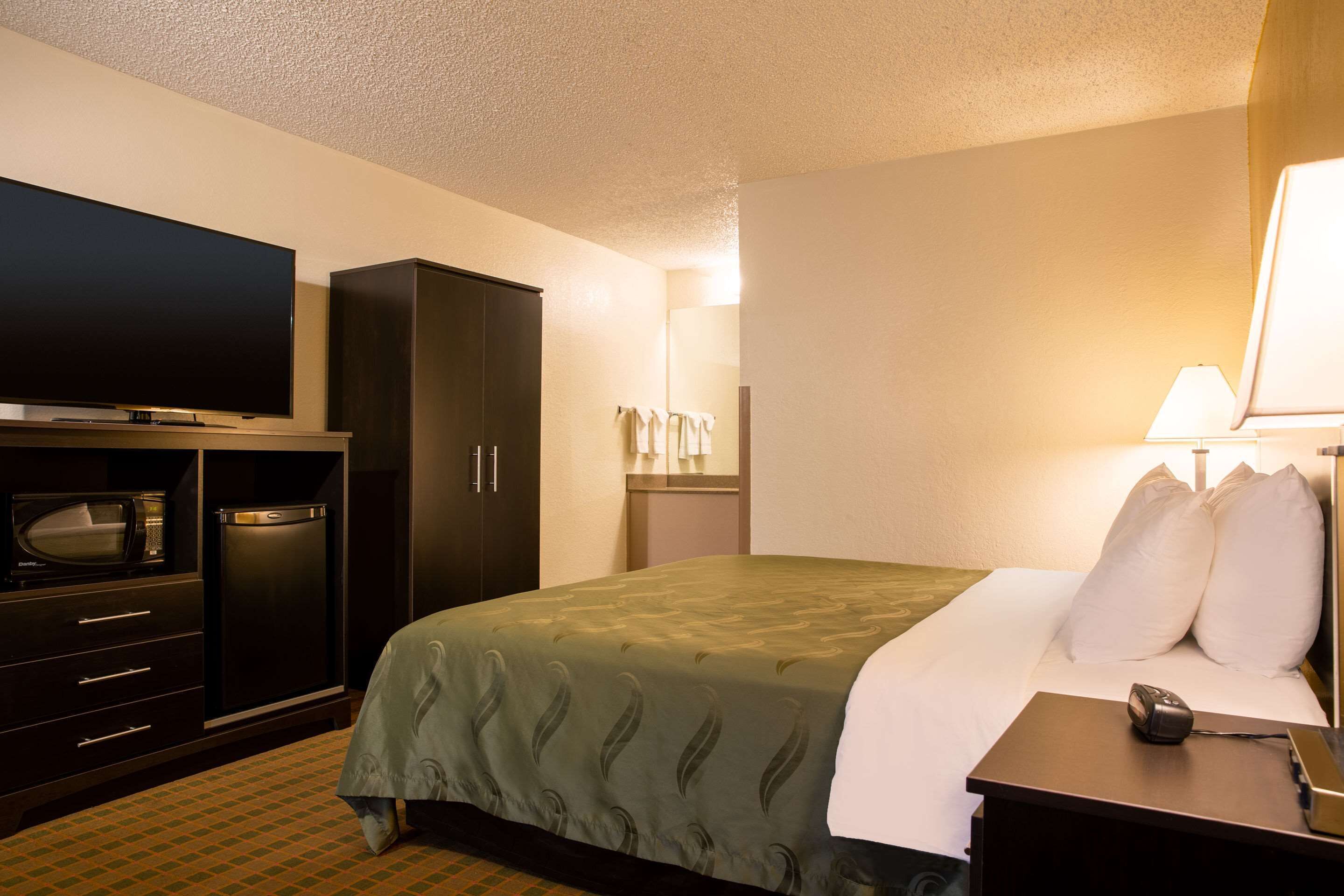 A hotel room with a bed, a television, a wardrobe, a desk with a lamp, and a microwave.