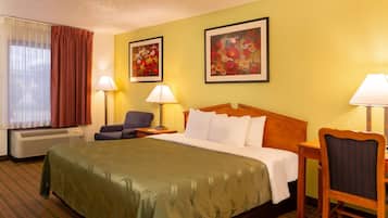 Une chambre d’hôtel avec un grand lit, deux tables de chevet avec des lampes, une chaise et deux tableaux représentant des motifs floraux, encadrés et accrochés au mur.