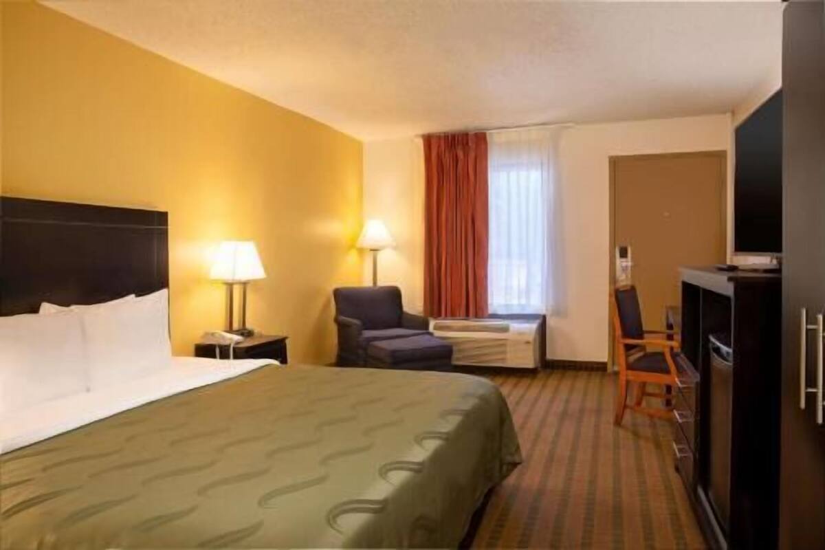 A hotel room with a bed, a desk, a chair, a TV, and a window with curtains.