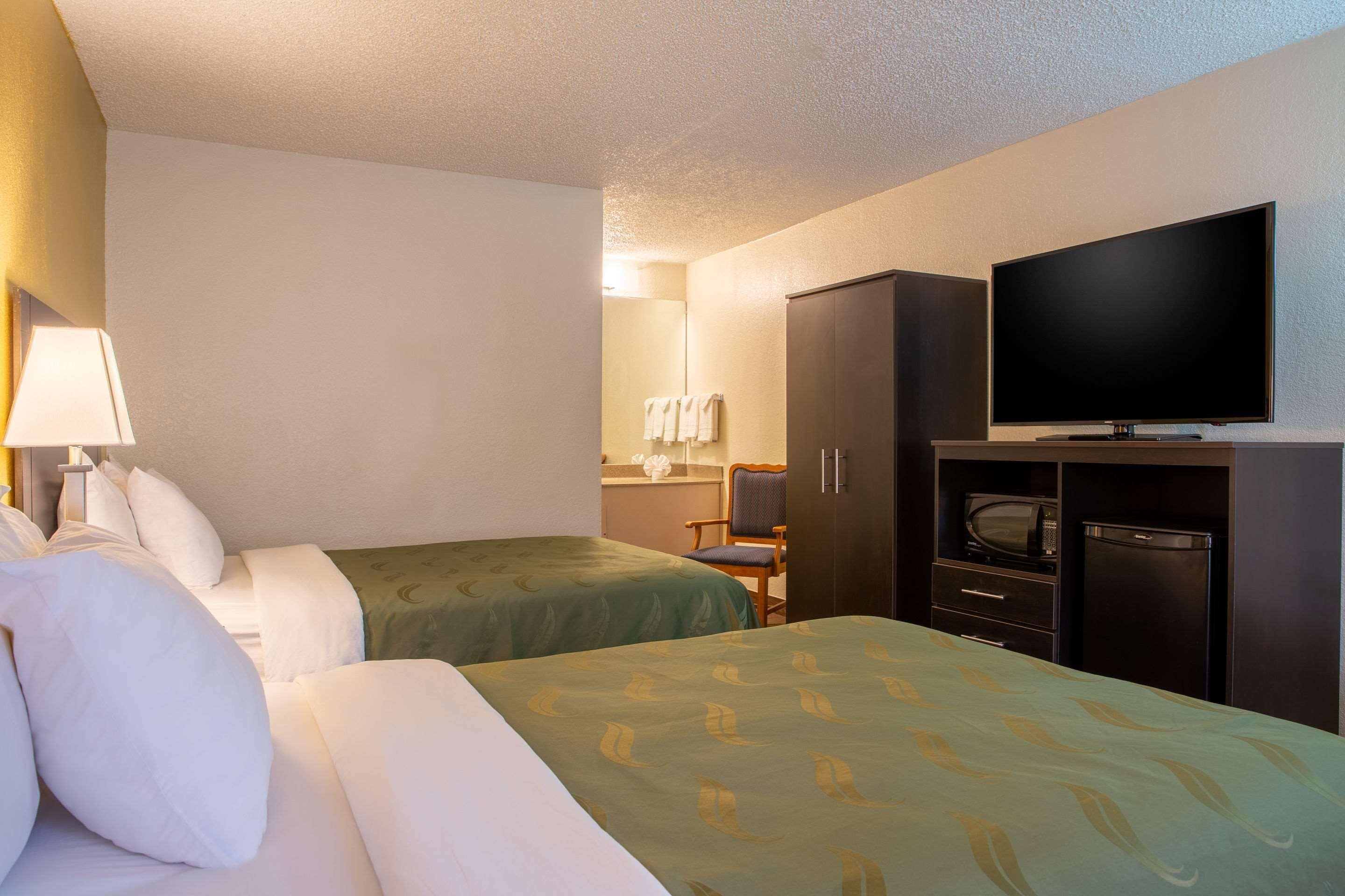 A hotel room with two beds, a television, a microwave, and a refrigerator.