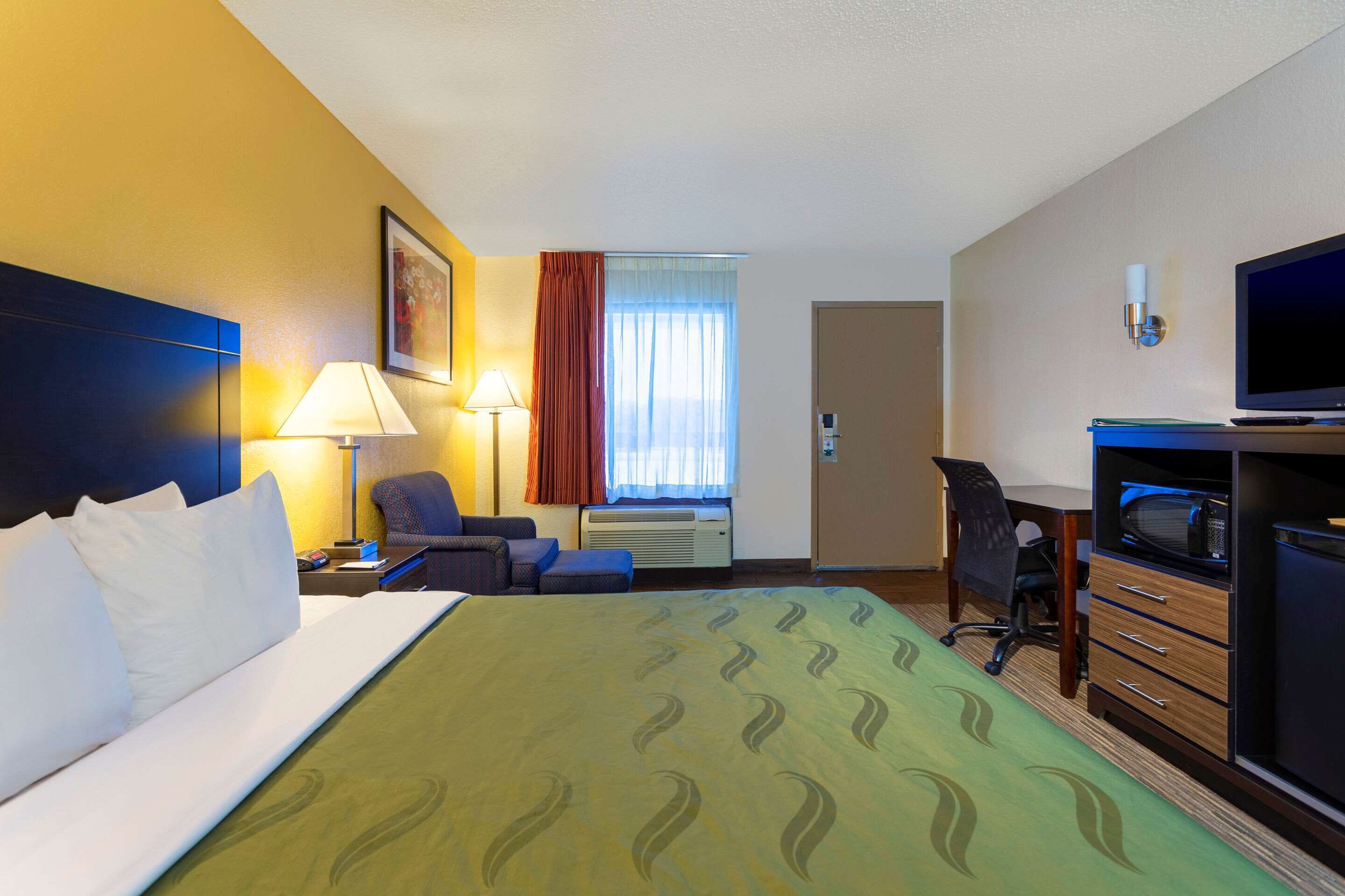 A hotel room with a bed, a desk, a chair, a television, and a window with curtains.