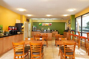 A restaurant with wooden tables and chairs, a kitchen area, and a view through large windows.