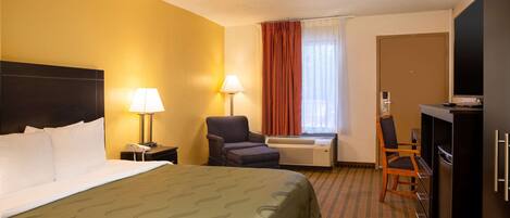Una habitación de hotel con cama, escritorio, silla, televisor y aire acondicionado.