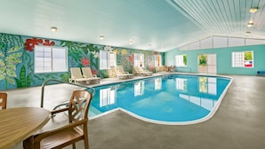 An indoor swimming pool with a mural, lounge chairs, and a table. - Quality Inn & Suites Big Stone Gap (Big Stone Gap)