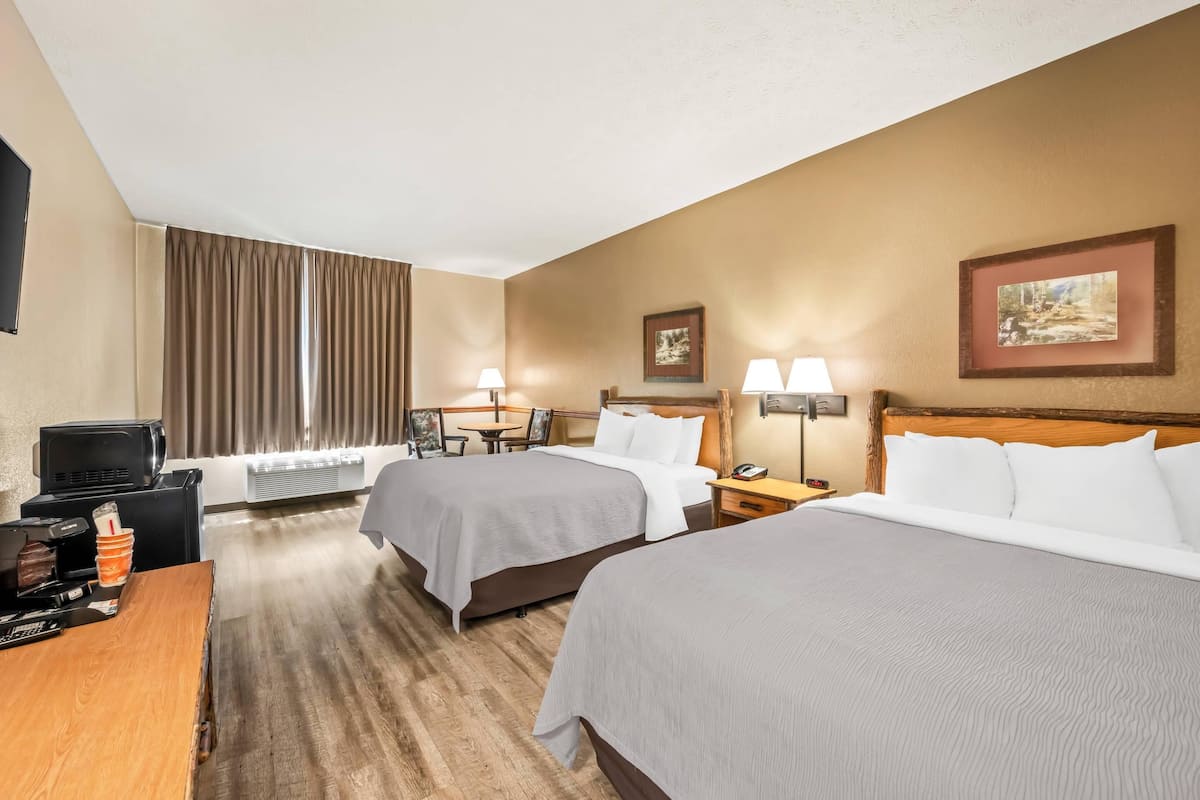 Quarto de hotel com duas camas, uma escrivaninha com cafeteira, televisão e janela com cortinas.