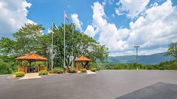 A gazebo with a red roof and two flagpoles, one with the American flag, in a parking lot with a mountain view.