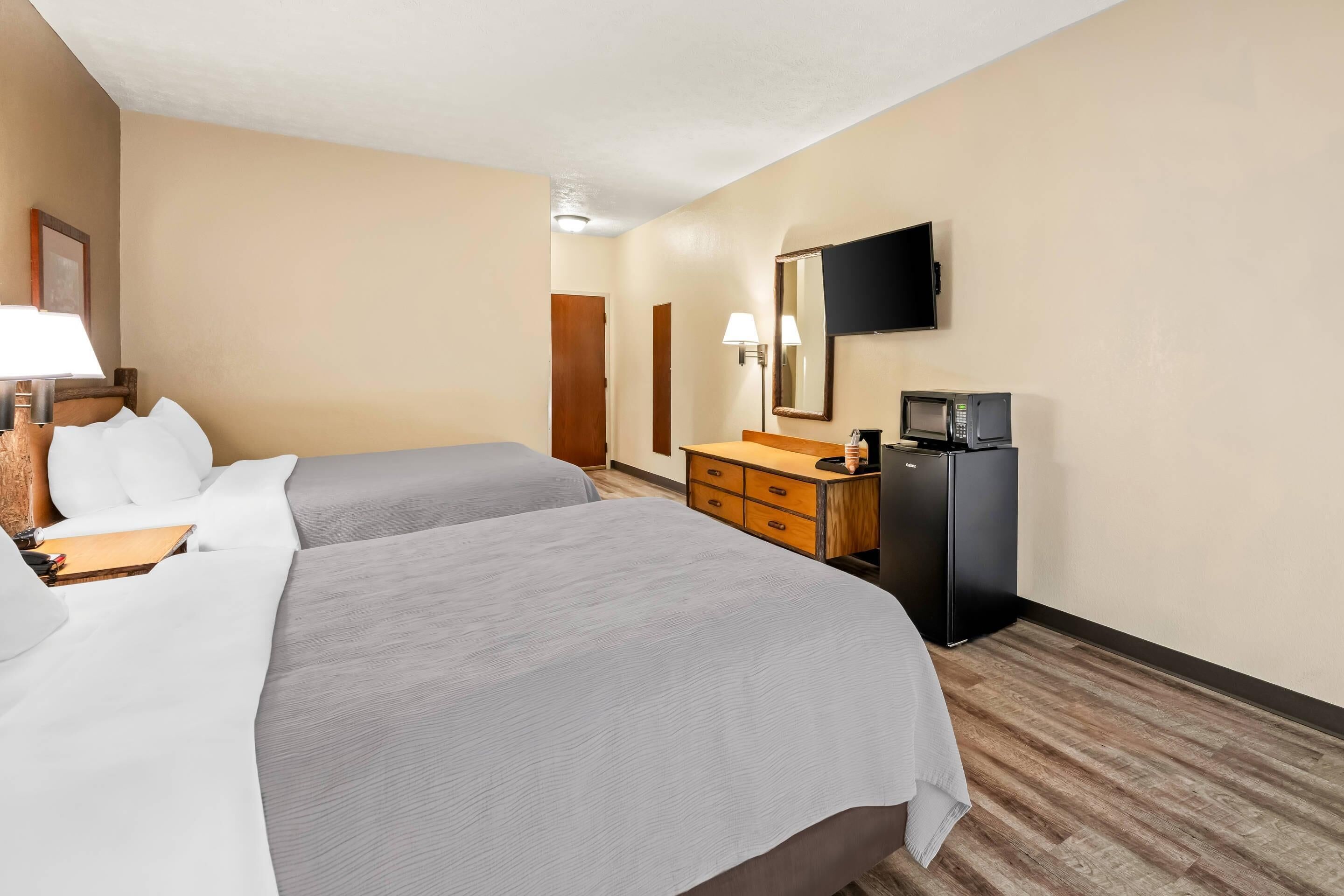 A hotel room with two beds, a desk, a dresser, a microwave, a TV, and a door.