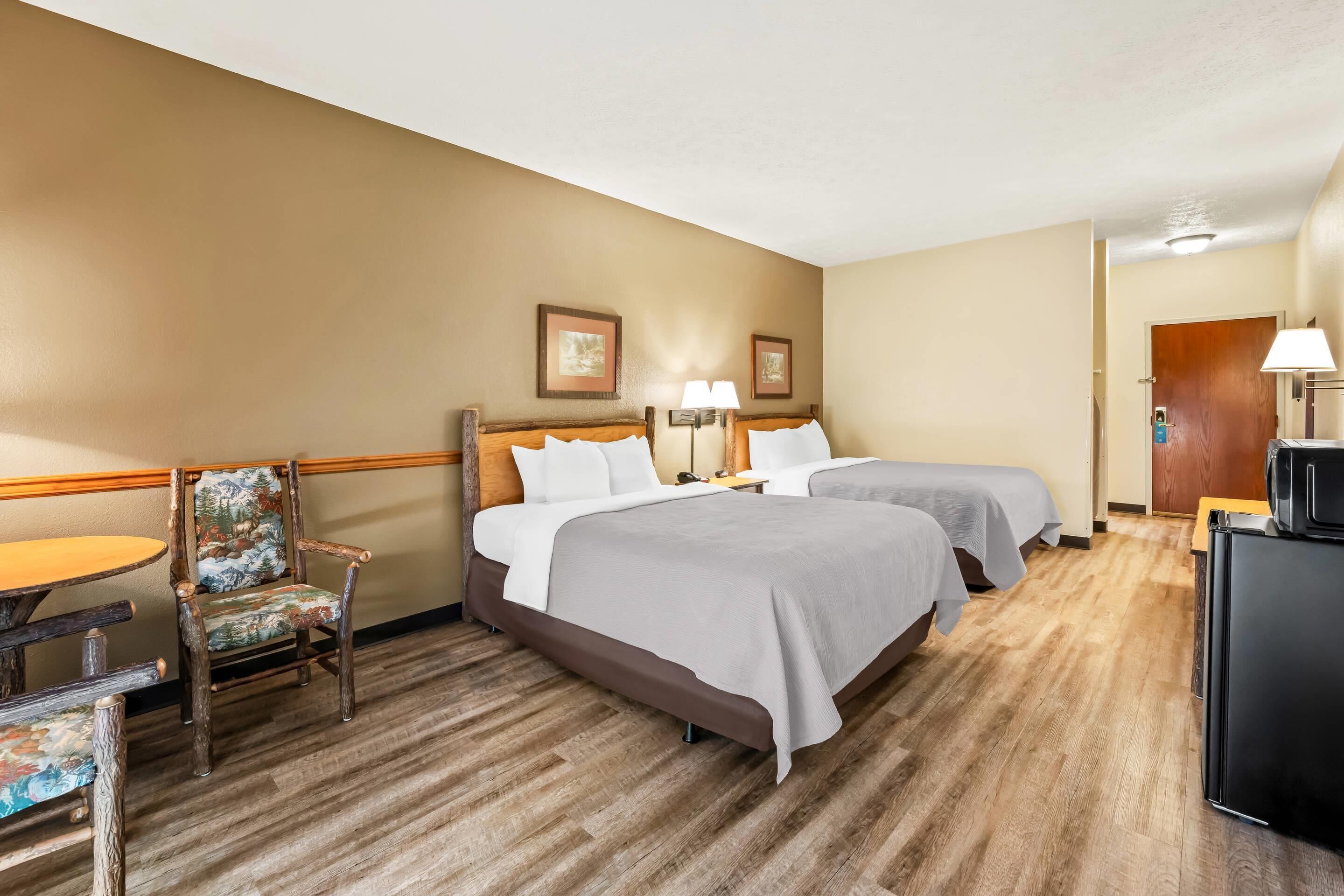 A hotel room with two beds, a wooden desk, a chair, and a refrigerator.