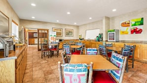 A restaurant with wooden tables and chairs, a buffet area, and a wall with food and drink advertisements. - Quality Inn & Suites Big Stone Gap (Big Stone Gap)