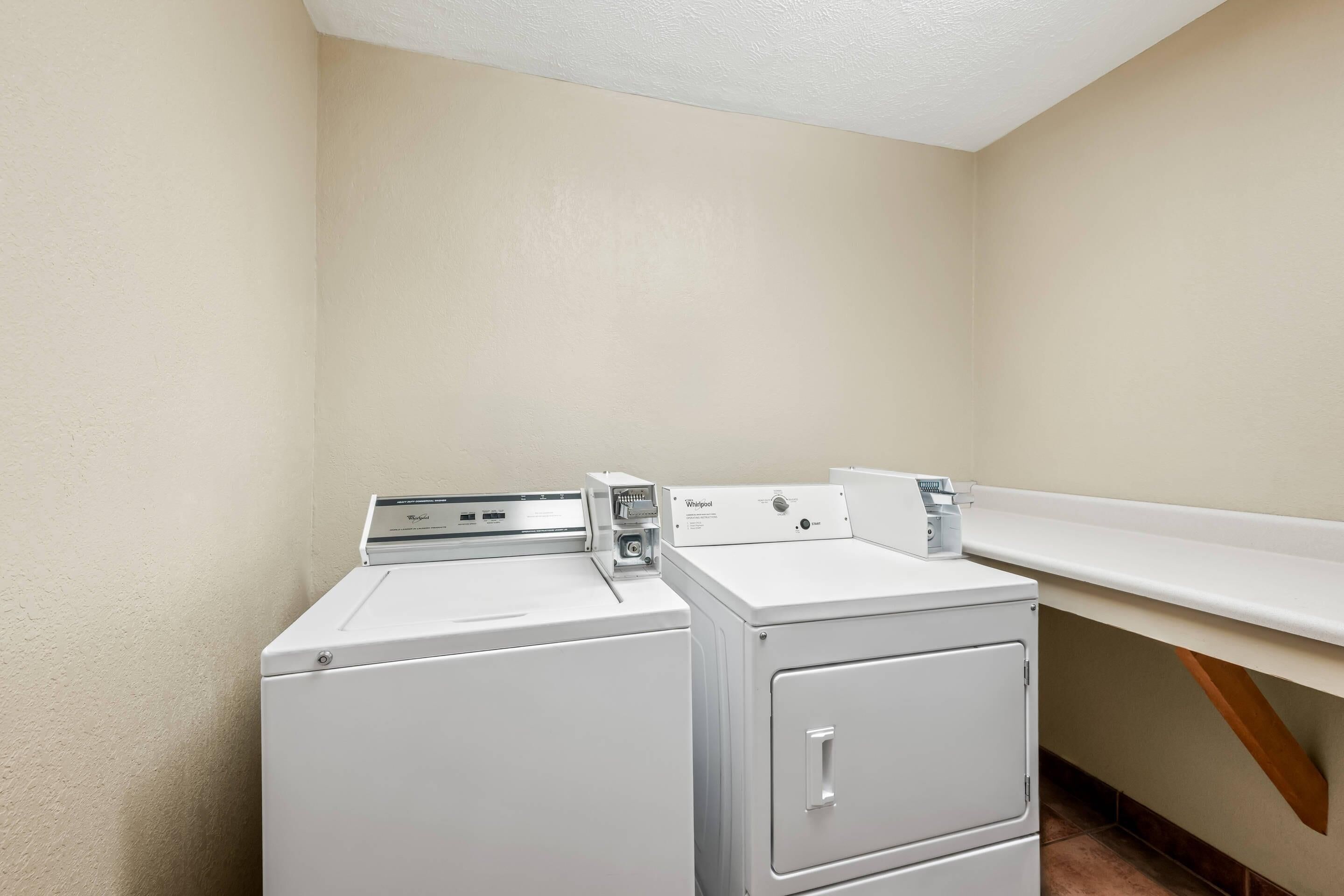A laundry room with two stacked washers and dryers, a white countertop, and a wooden beam.