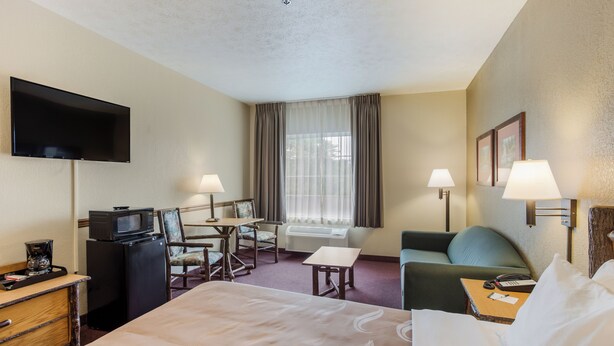 A hotel room with a bed, a desk with a computer, a TV, a coffee maker, and a window with curtains. - Quality Inn & Suites Big Stone Gap (Big Stone Gap)