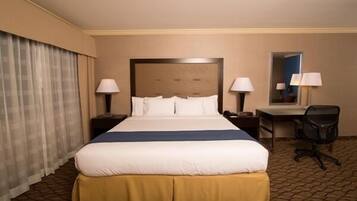 Habitación de hotel con una cama grande, dos mesitas de noche con lámparas, un escritorio con silla y un espejo en la pared.