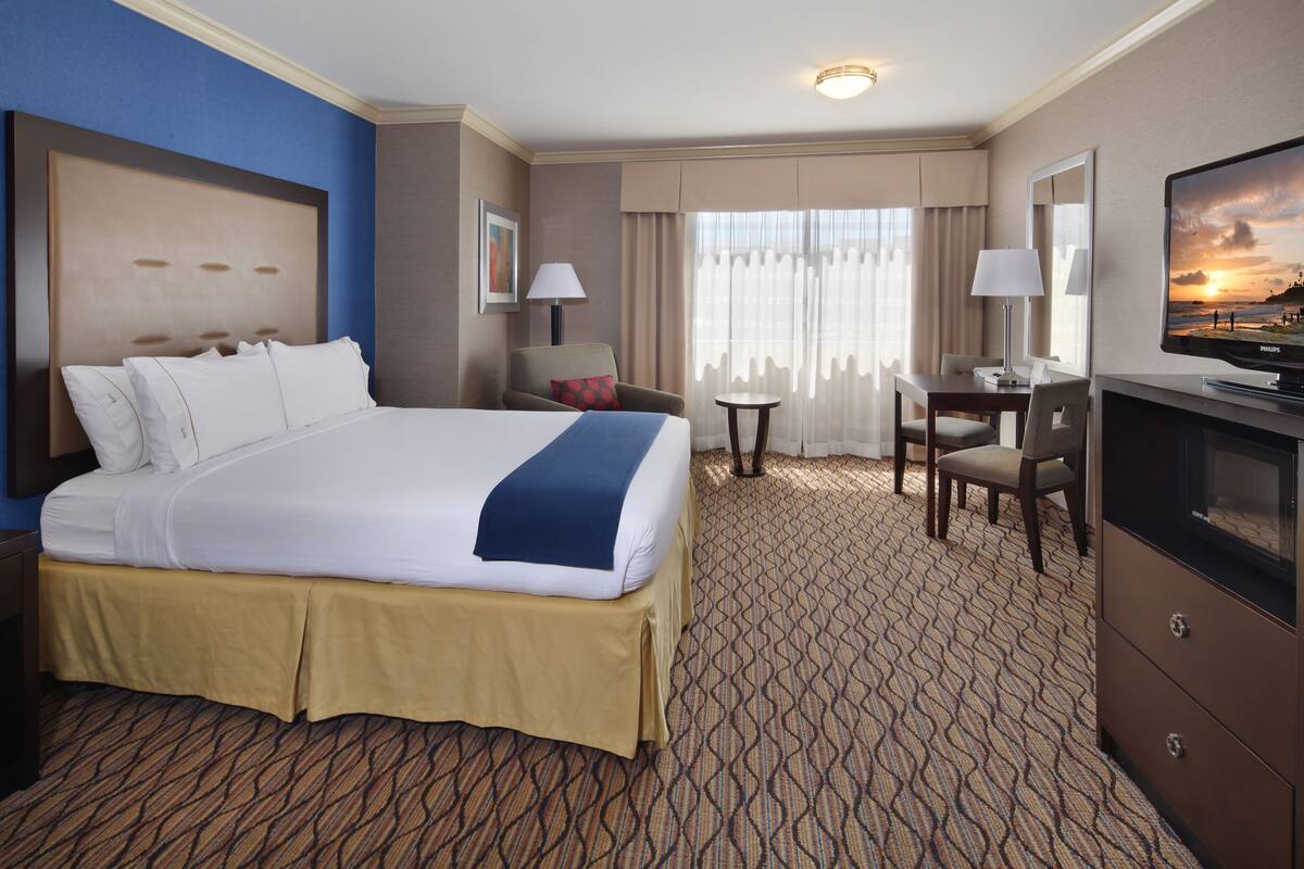 A hotel room with a large bed, a desk, a chair, a television, and a window with curtains.