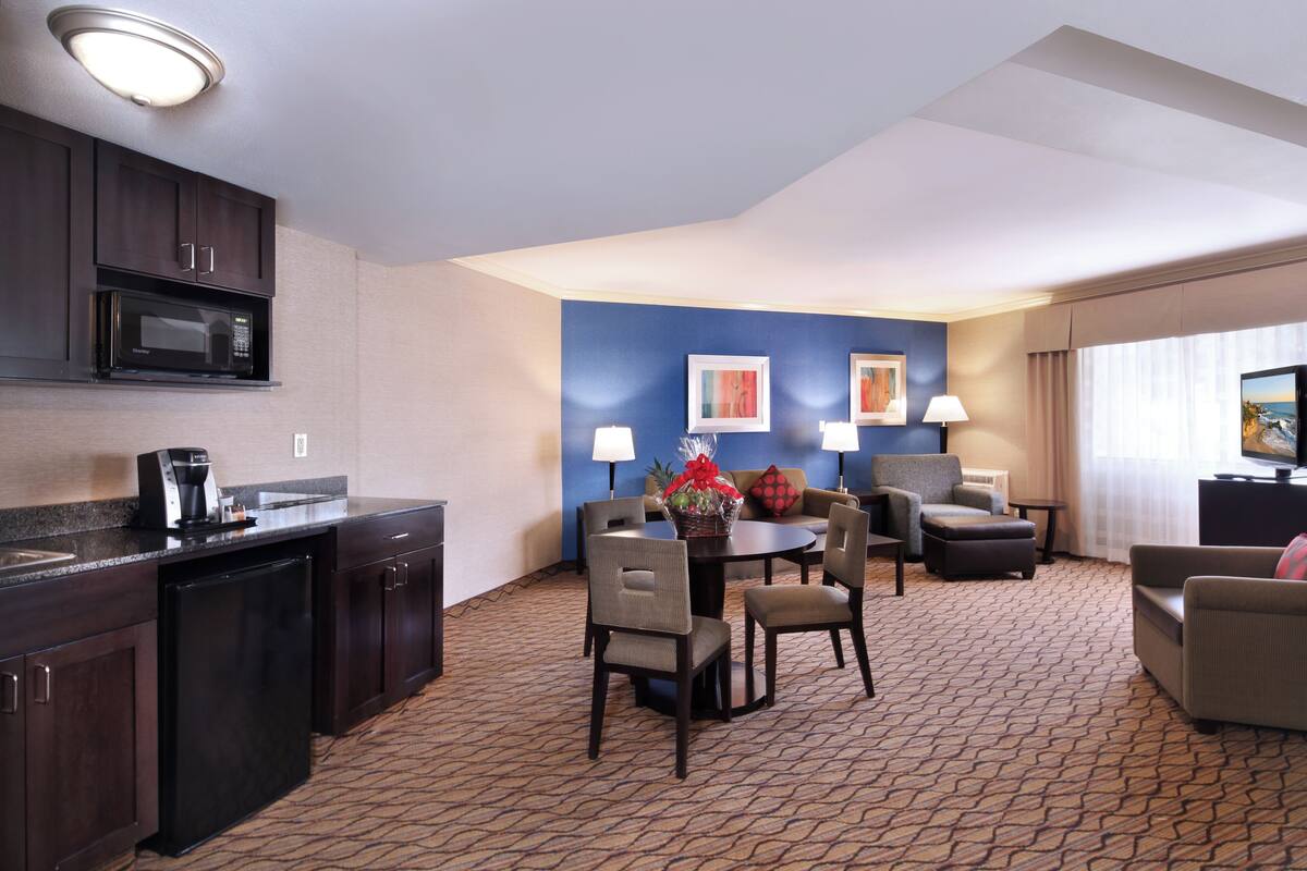 A hotel room with a kitchenette, dining area, and seating space.