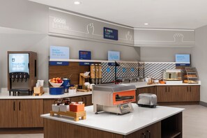 A breakfast area with a coffee machine, fruit bowl, cereal, and a hot food station. - Holiday Inn Express Port Hueneme by IHG (Port Hueneme)
