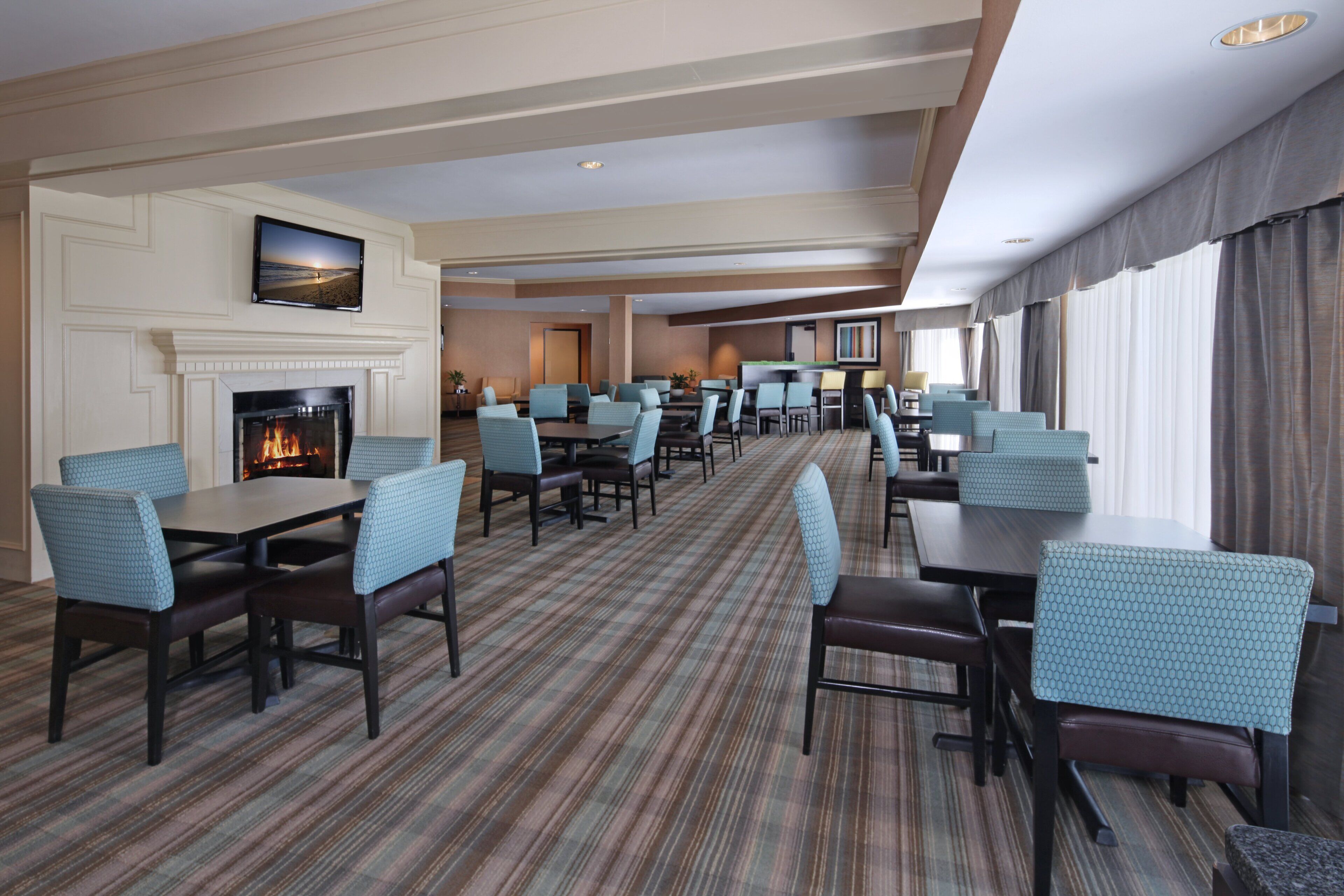 A hotel lobby with a fireplace, multiple seating areas, and a television screen.