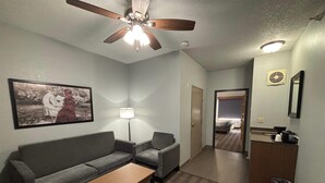 A compact living room with a sofa, two armchairs, a coffee table, a ceiling fan, and a framed picture on the wall. - AmericInn by Wyndham Galesburg (Galesburg)