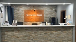 A reception desk with a stone wall backdrop, a sign reading "AmerInn by Wyndham", and various amenities like a clock, a small plant, and a framed picture. - AmericInn by Wyndham Galesburg (Galesburg)