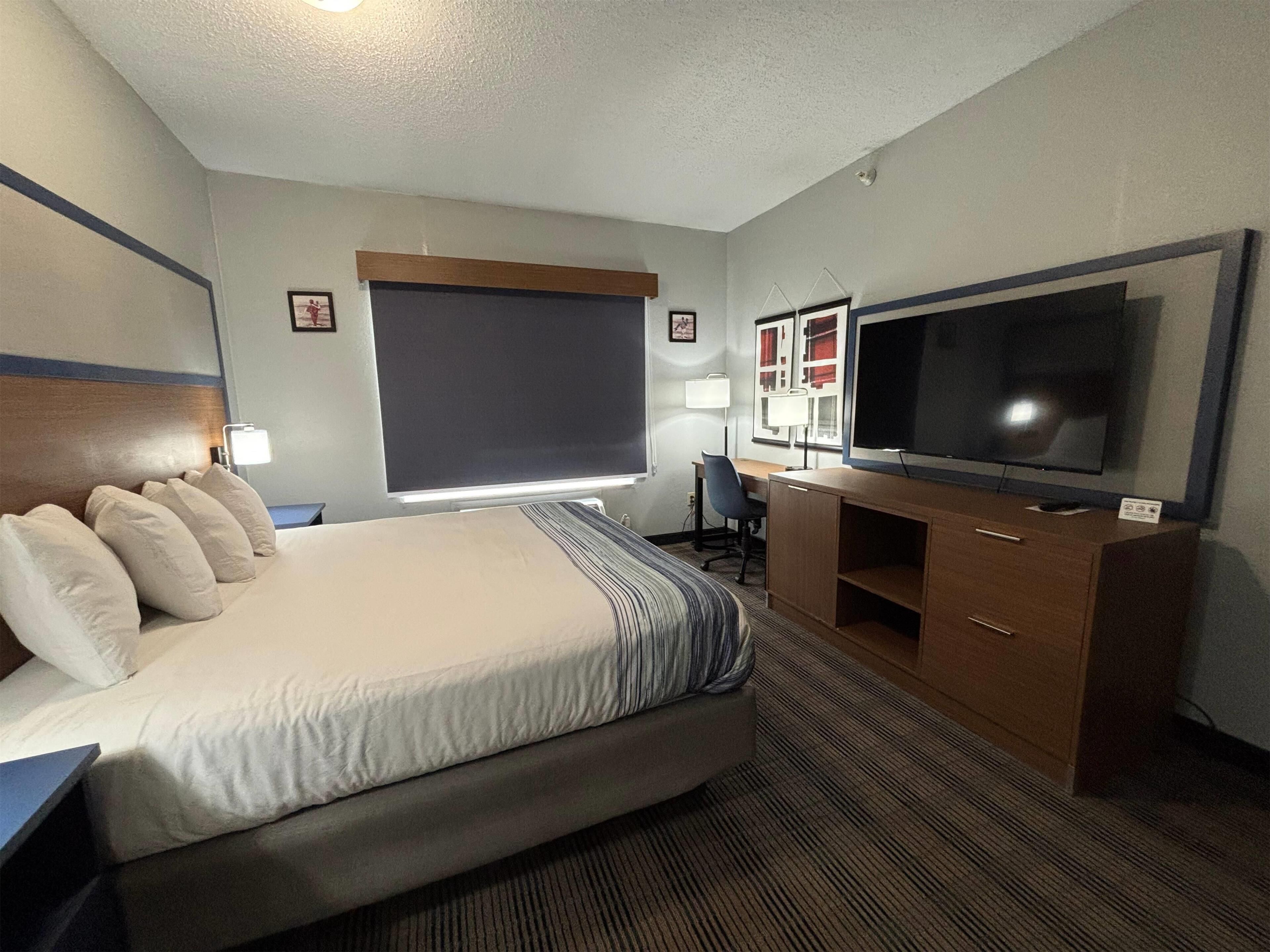 A hotel room with a large bed, a desk, a TV, and a window.