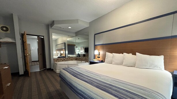 A hotel room with a large bed, a bathroom with a bathtub, and a mirror. - AmericInn by Wyndham Galesburg (Galesburg)