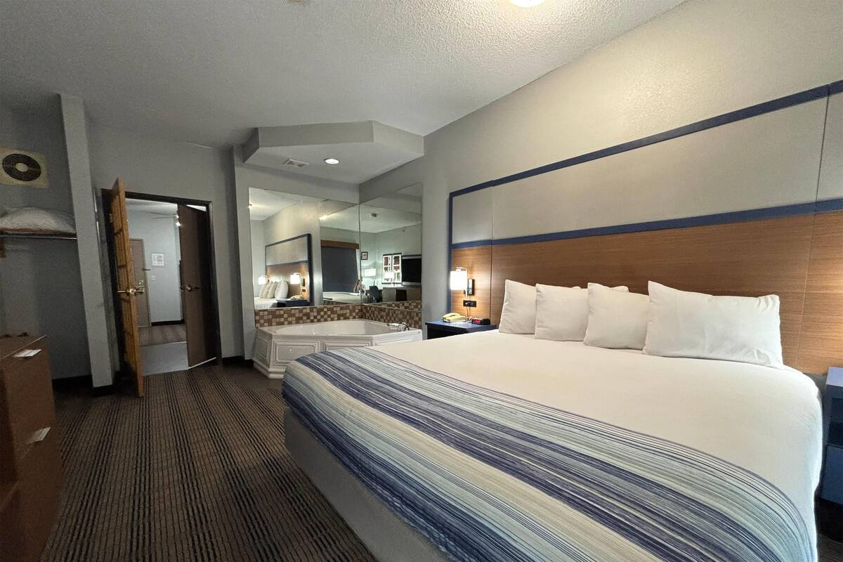 A hotel room with a large bed, a bathroom with a bathtub, and a mirror.