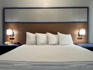 Ein Hotelzimmer mit einem großen Bett, vier Kissen, zwei Nachttischen mit Lampen sowie einem Beistelltischchen mit Telefon und einer digitalen Uhr.