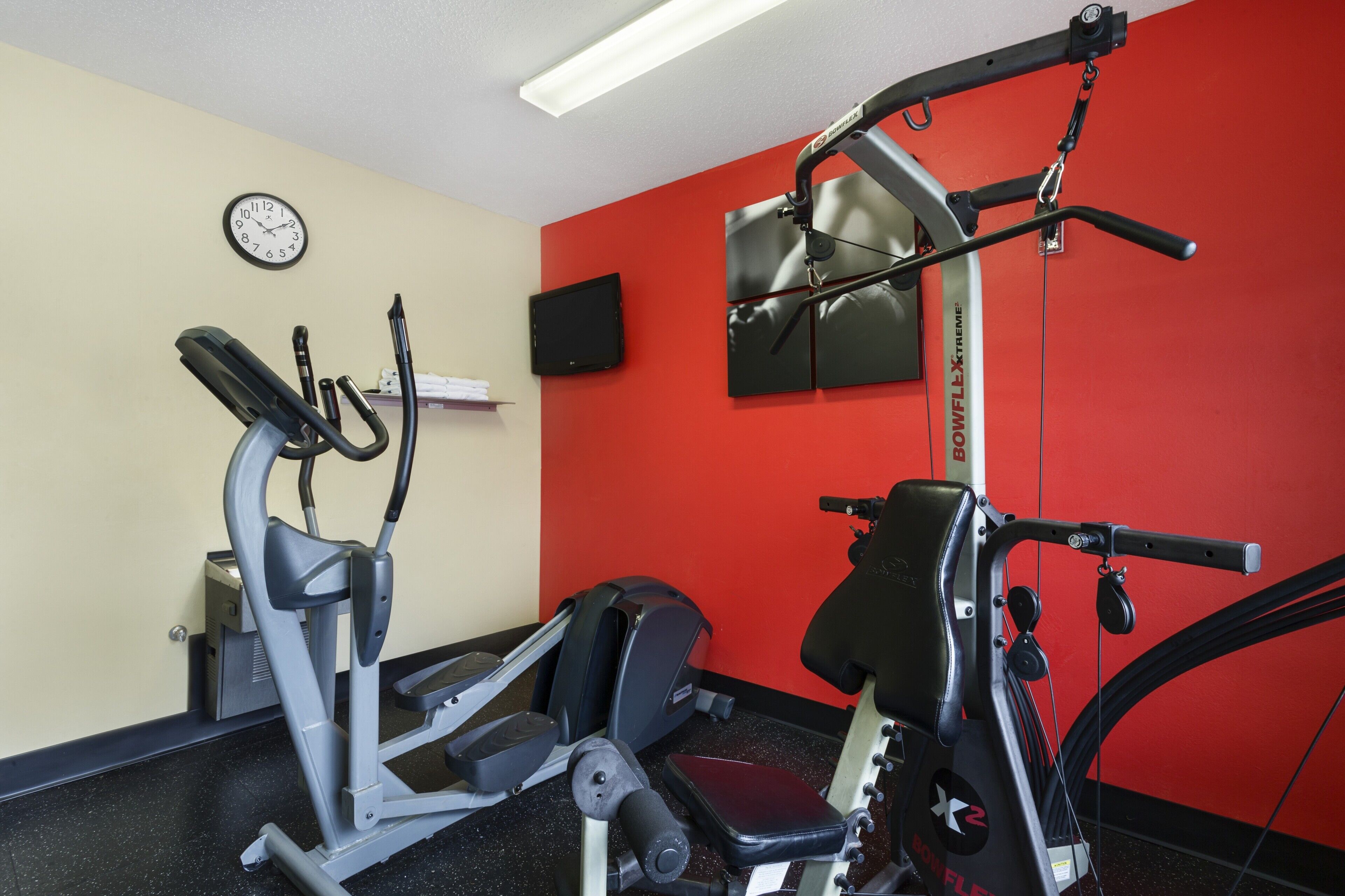 A gym with exercise equipment, a clock, and a television on the wall.