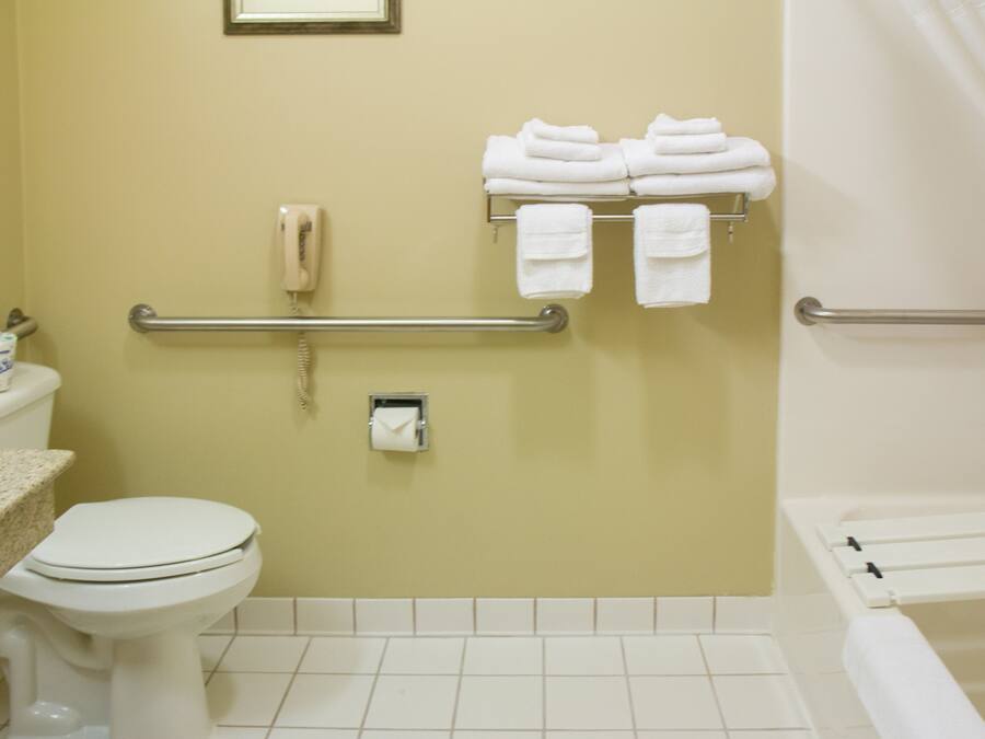 A bathroom with a toilet, a towel rack with folded towels, a hand dryer, and a grab bar.