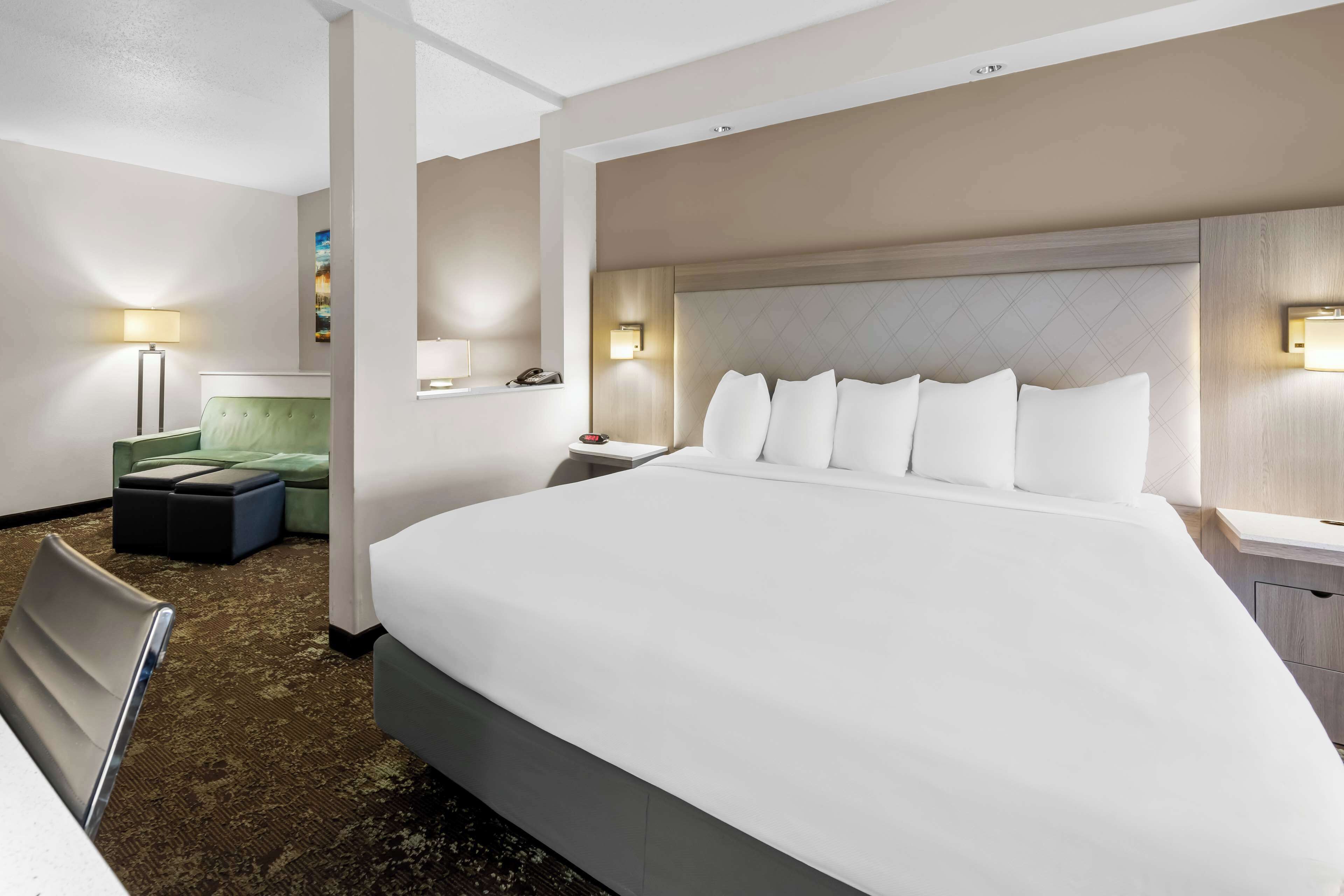 A hotel room with a large bed, a desk, a chair, and a small sofa.