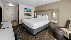 A hotel room with a large bed, a desk with a laptop, a chair, a small ottoman, and a painting on the wall. - Best Western Worlds of Fun Inn & Suites (Kansas City)