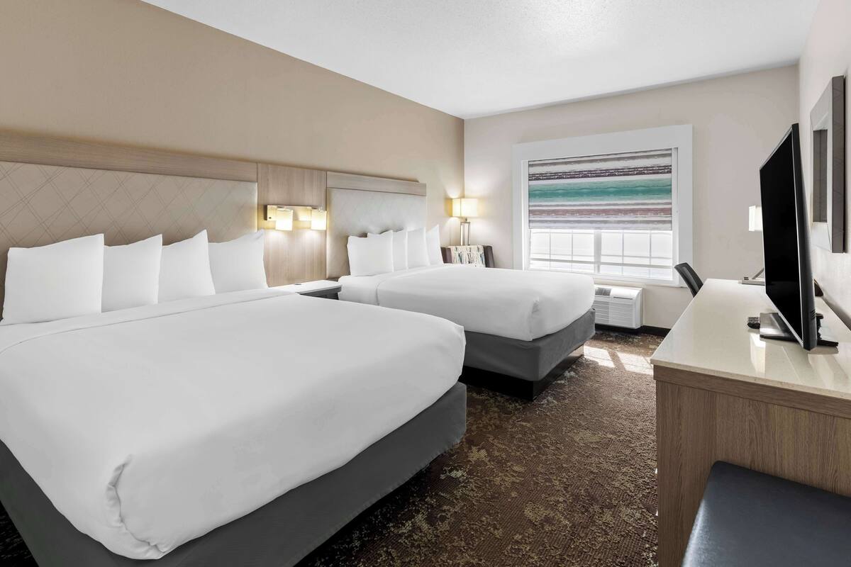 A hotel room with two beds, a desk, a TV, and a window with a view.
