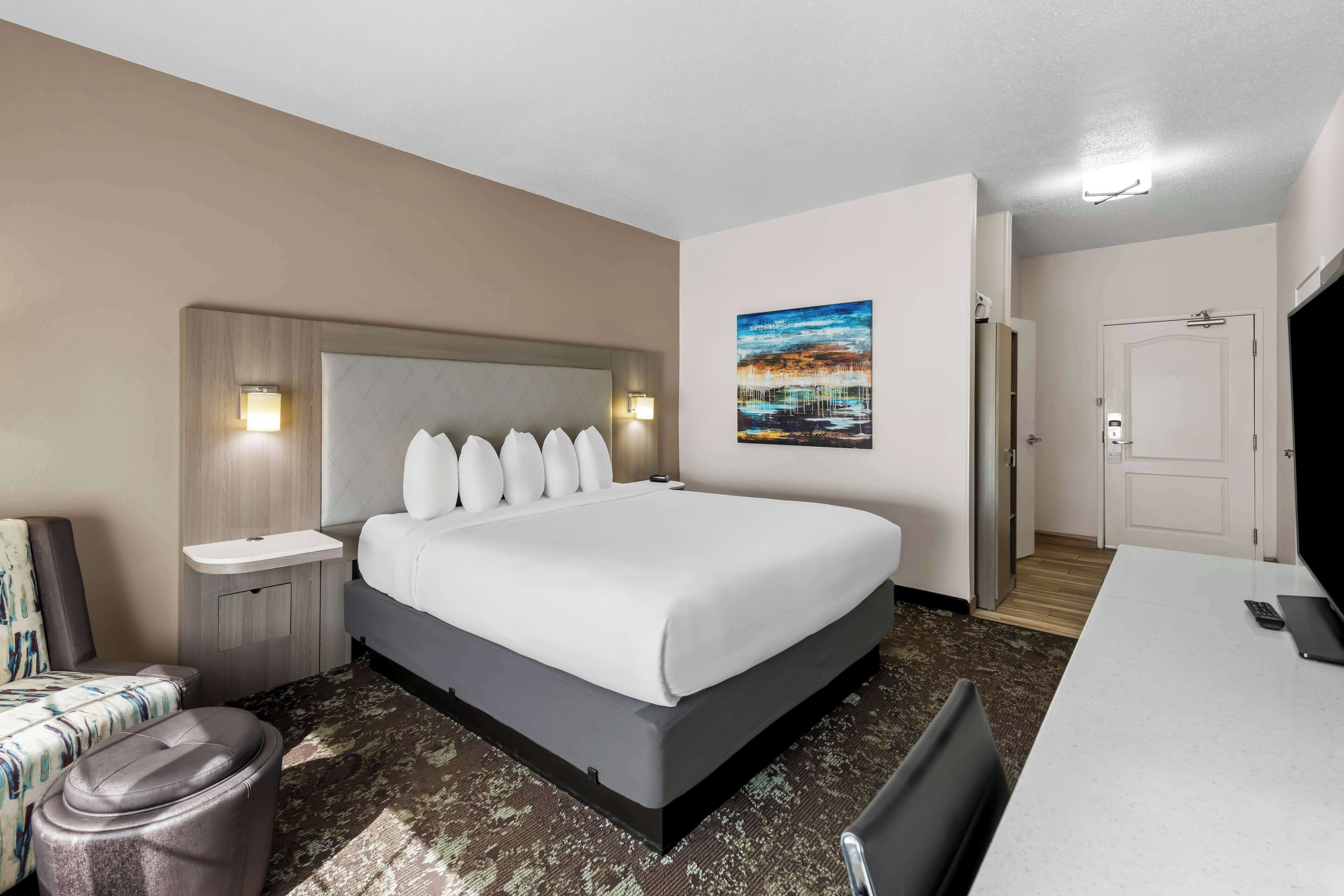 Une chambre d’hôtel avec un grand lit, une table de chevet, une chaise, un bureau et un tableau au mur.