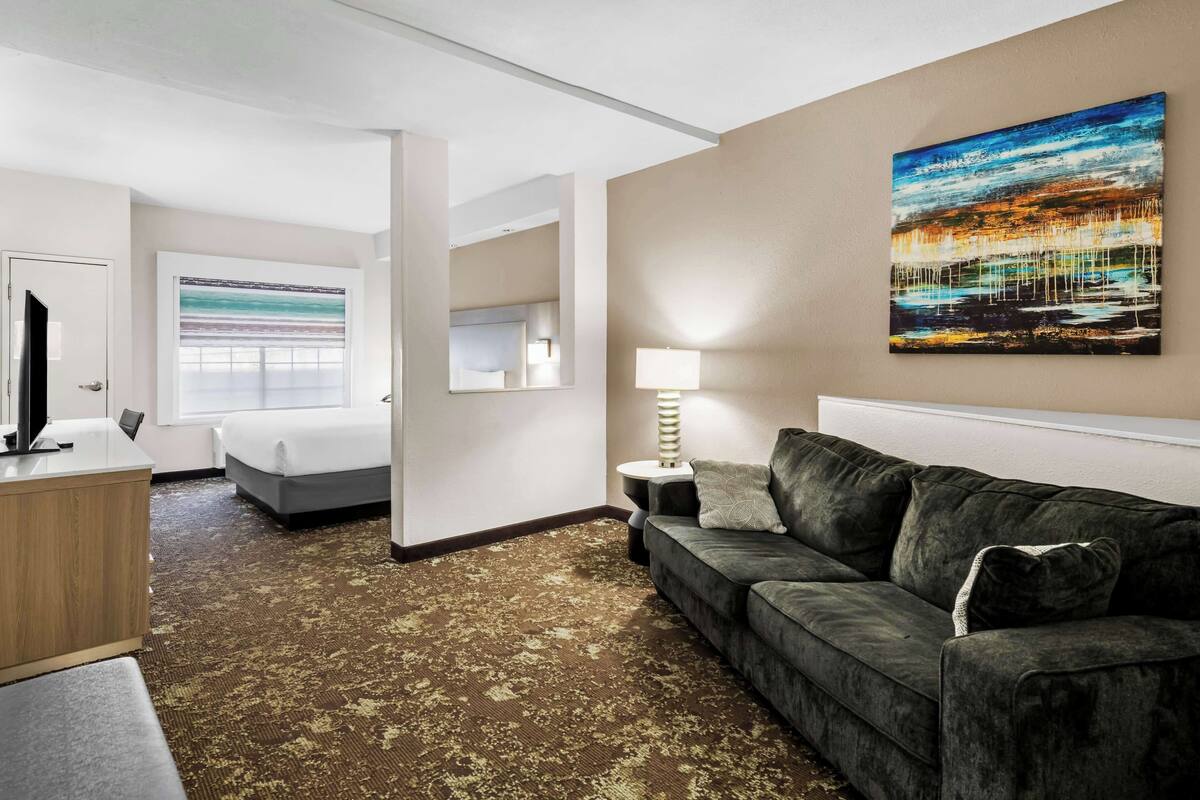 A hotel room with a bed, a sofa, a desk, a lamp, and a painting on the wall.