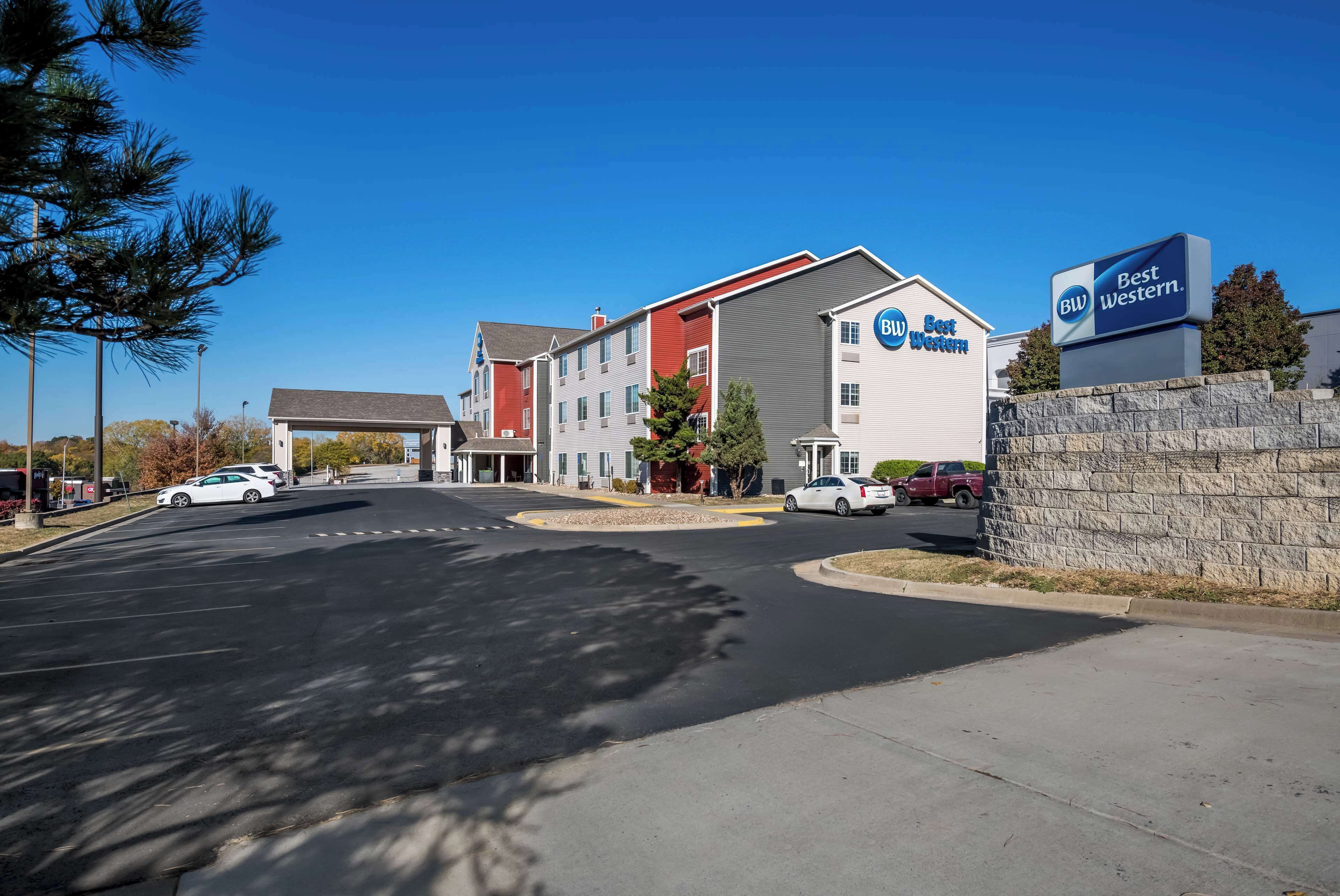 A Best Western hotel with a parking lot, a stone wall, and a clear blue sky.