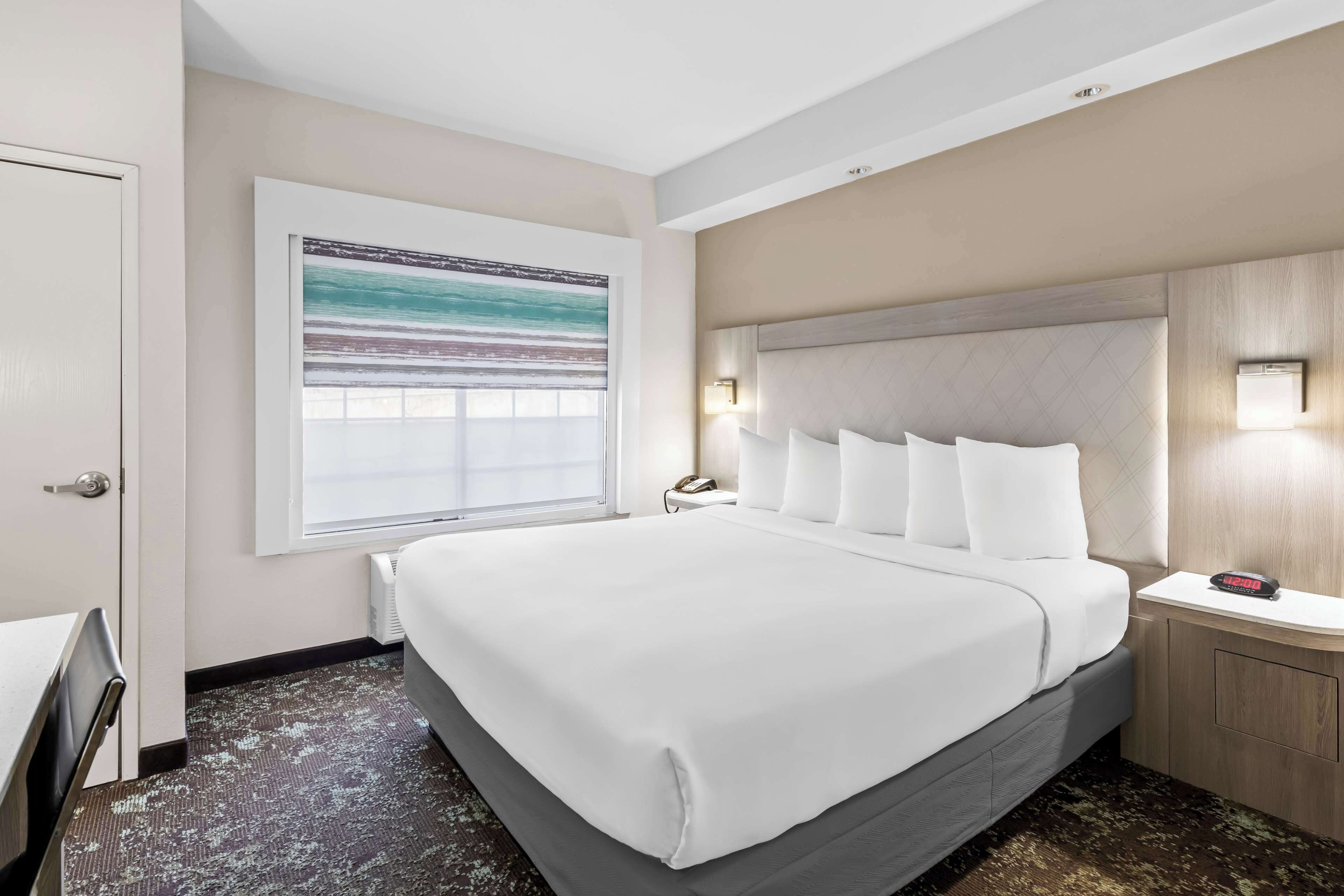 A hotel room with a large bed, a nightstand, a desk, and a window with a view.