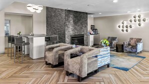 A modern living room with a herringbone wood floor, a fireplace, a bar area, and a seating arrangement with patterned sofas and chairs. - Best Western Worlds of Fun Inn & Suites (Kansas City)