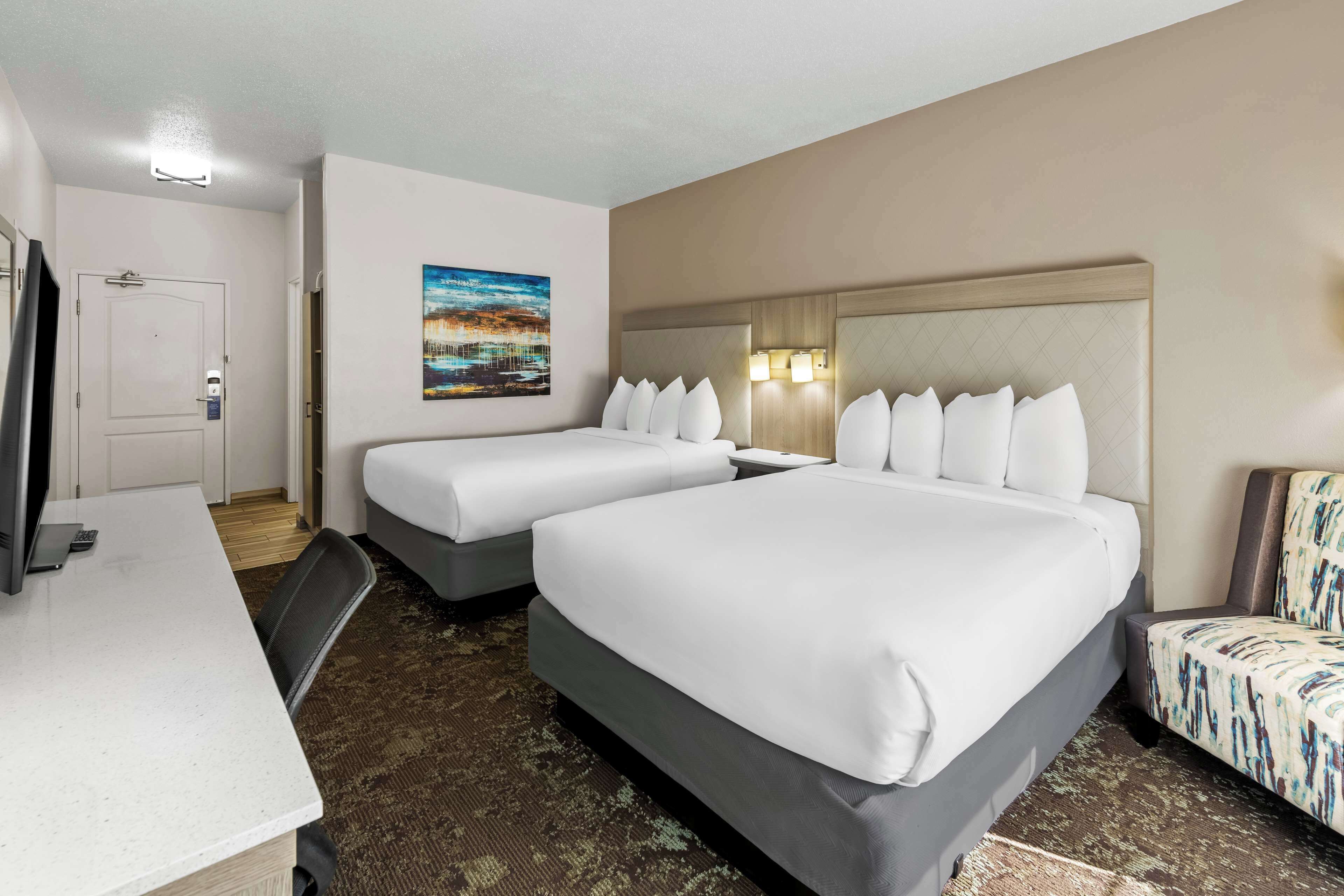 A hotel room with two beds, a desk, a TV, and a painting on the wall.